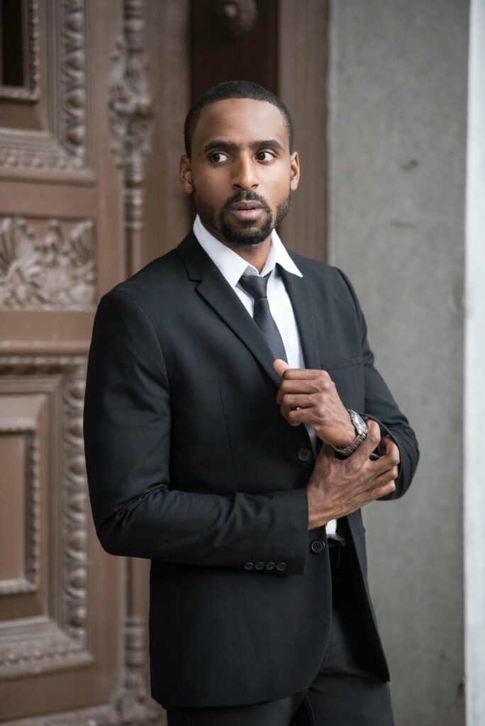 Elegant man in a black suit posing confidently outdoors with a serious expression.